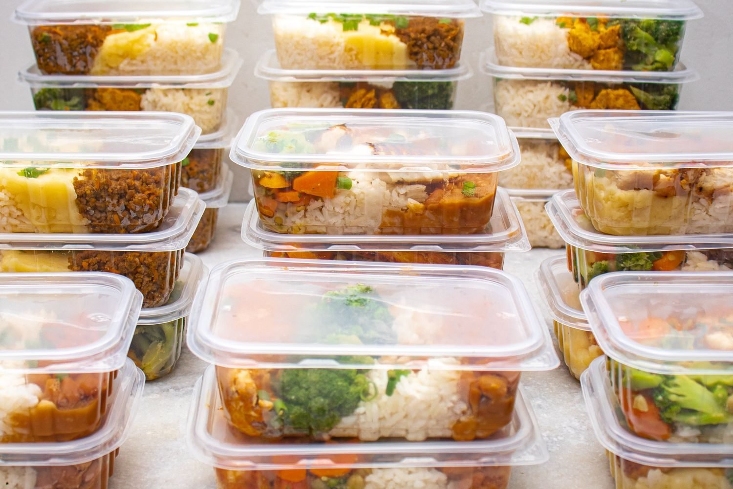 Person preparing a vegetarian meal prep with dal, paneer, and vegetables in glass containers
