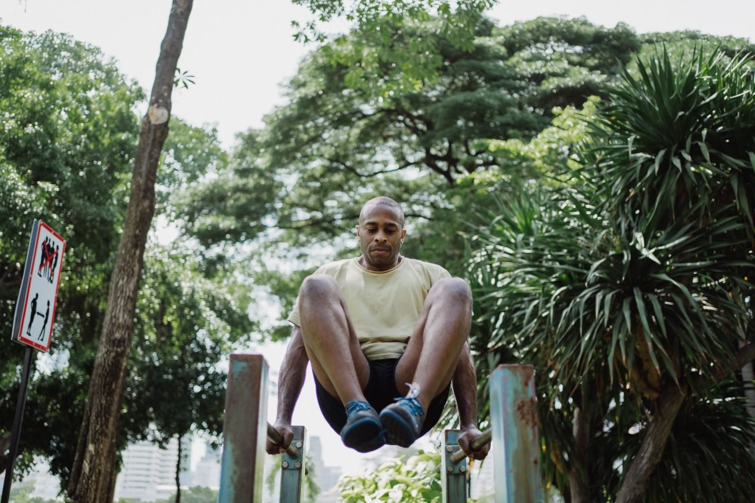 Man performing a hanging leg raise on parallel bars outdoors