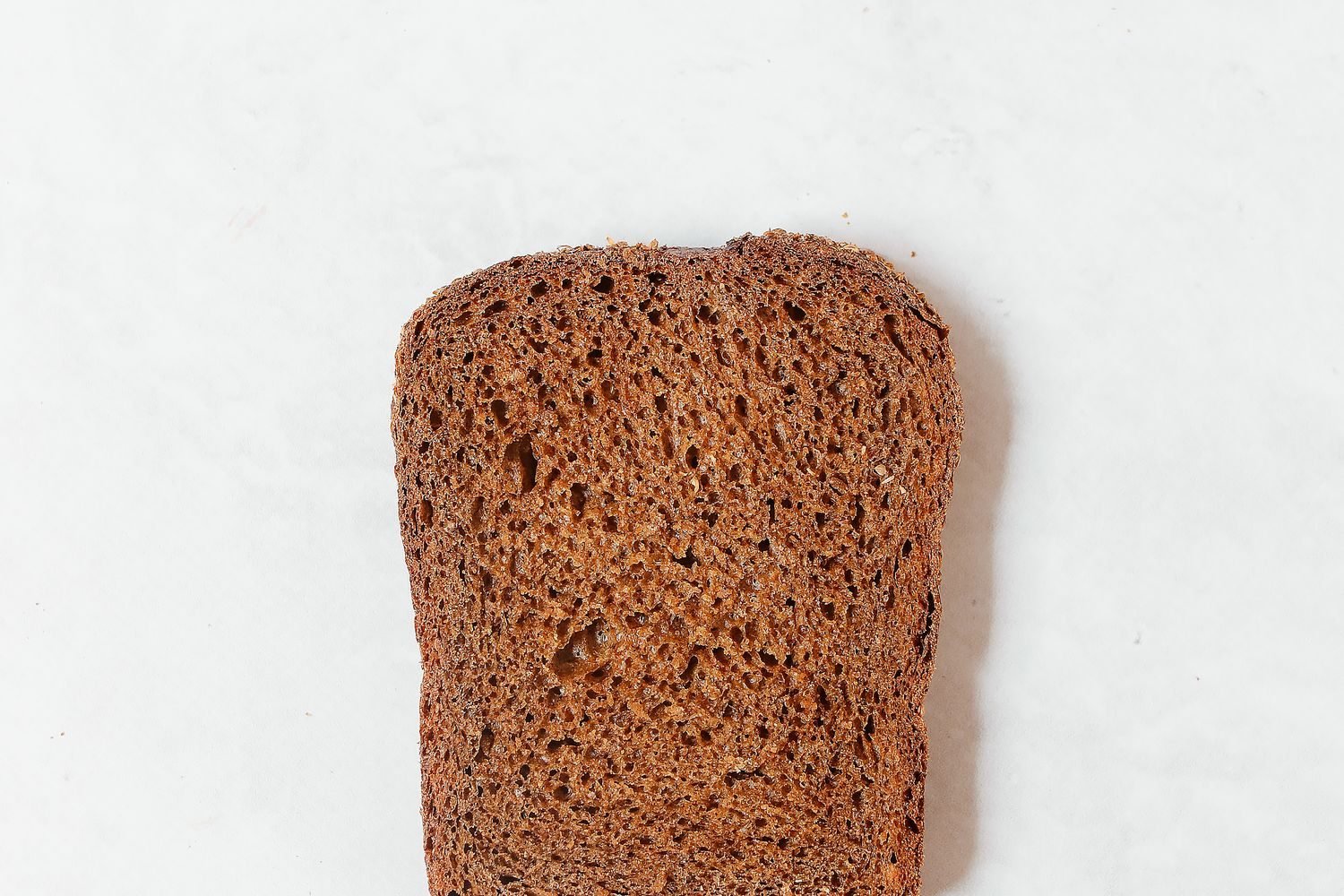 A slice of gluten-free bread showing crumb structure next to a small bowl of xanthan gum powder