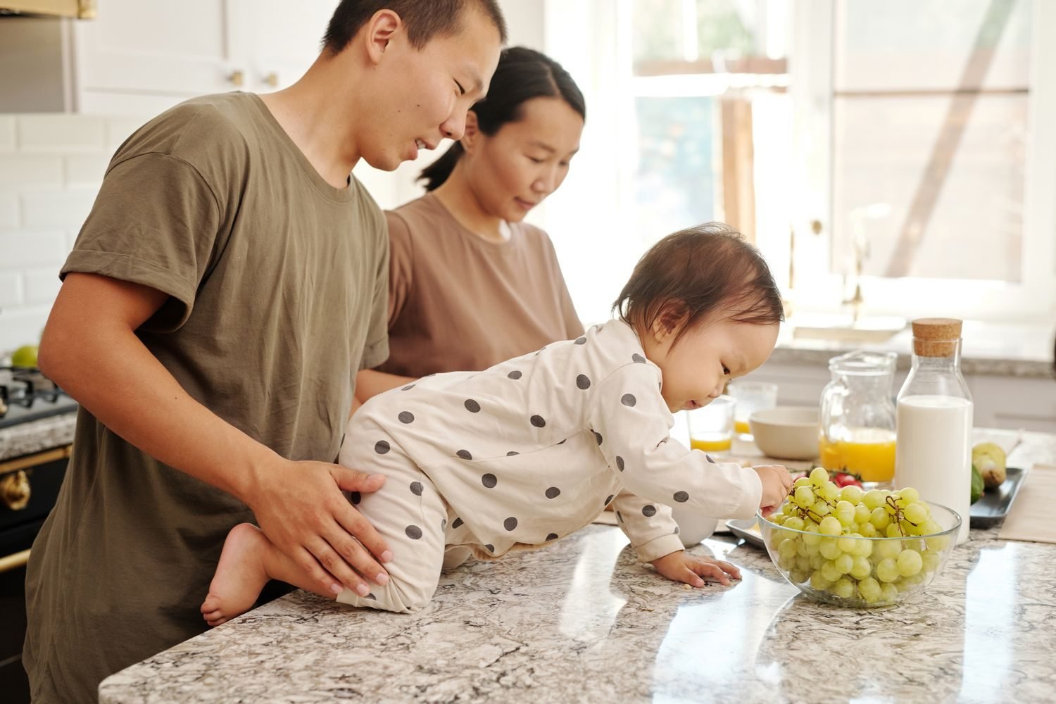 Toddler drinking whole milk from a cup at the kitchen table with fruit and vegetables on the plate
