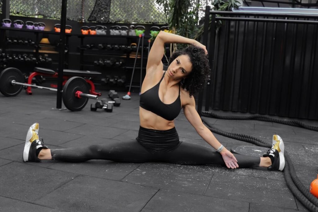 Woman stretching on the floor of a gym surrounded by kettlebells and dumbbells