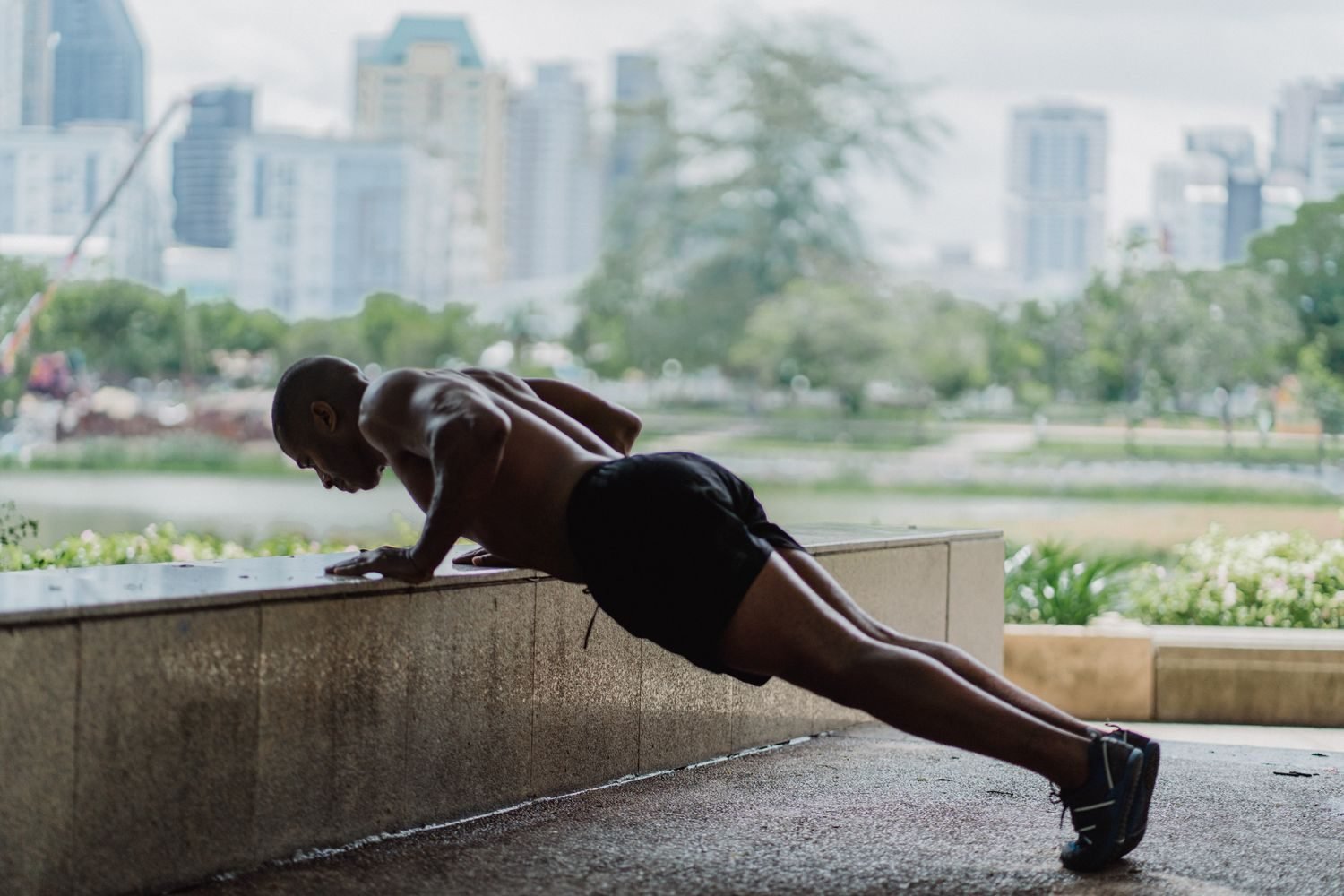 Man doing an outdoor push-up on a ledge with a city skyline behind him