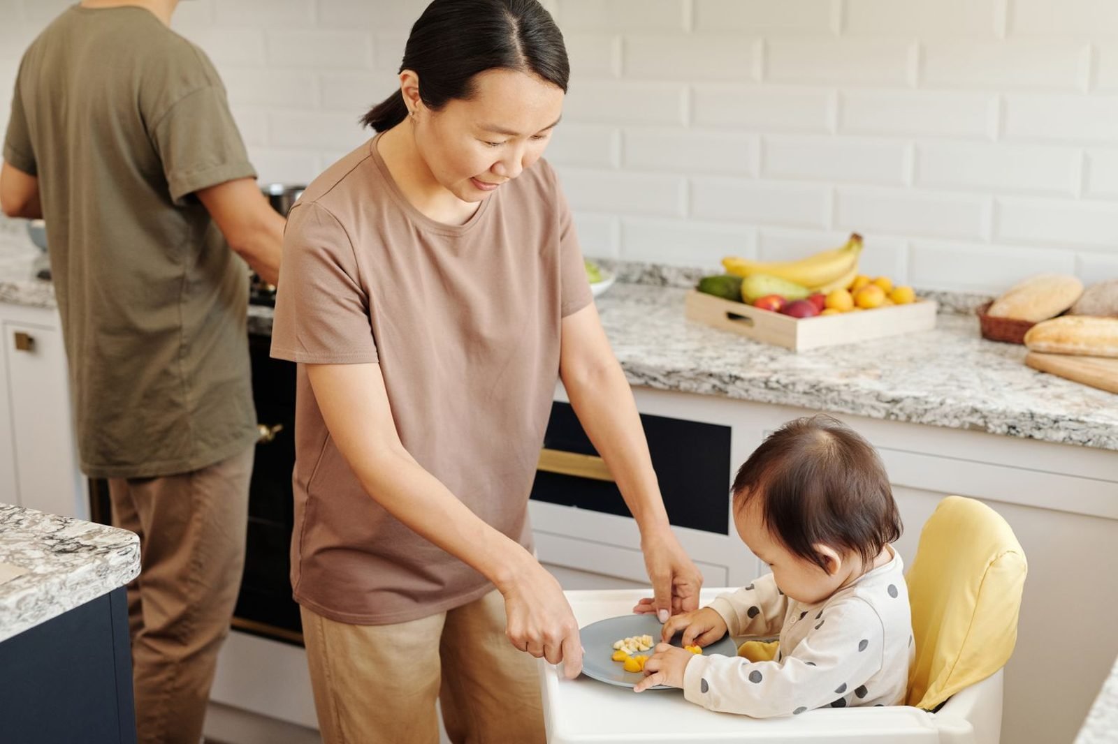 Toddler eating a colorful plate of fruits and vegetables at a family table