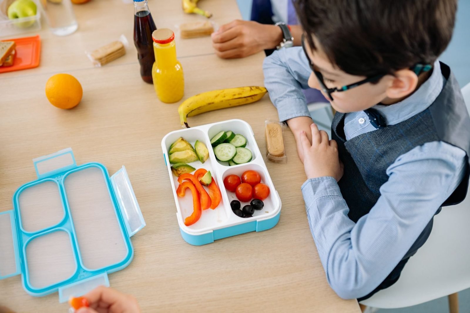Parent and school-age child preparing a balanced lunch box with fruits, grains, and protein