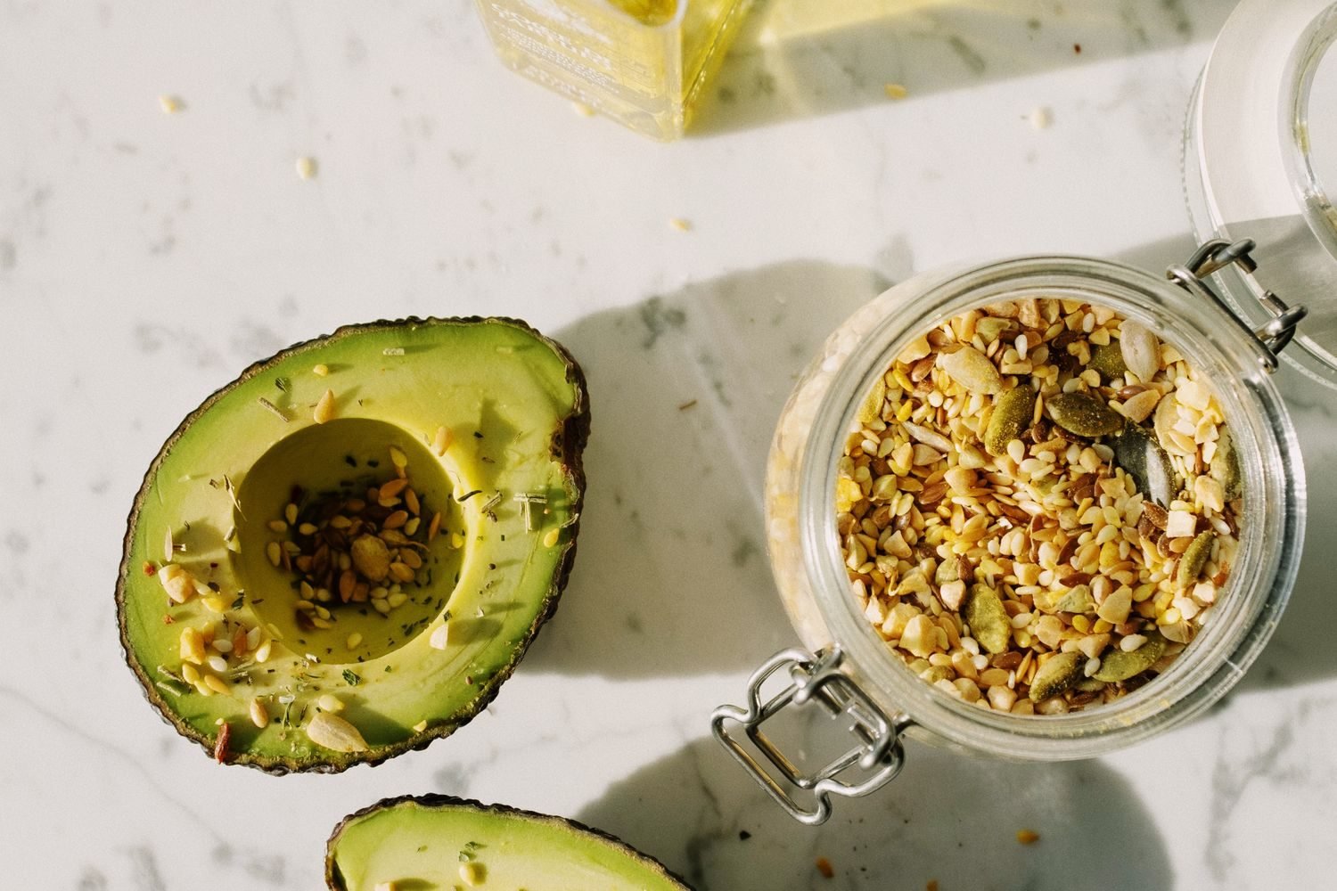 Assortment of healthy fat sources including avocado, olive oil, nuts, and salmon on a wooden table