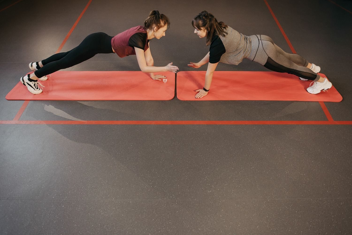 Two women doing a plank exercise together on gym mats