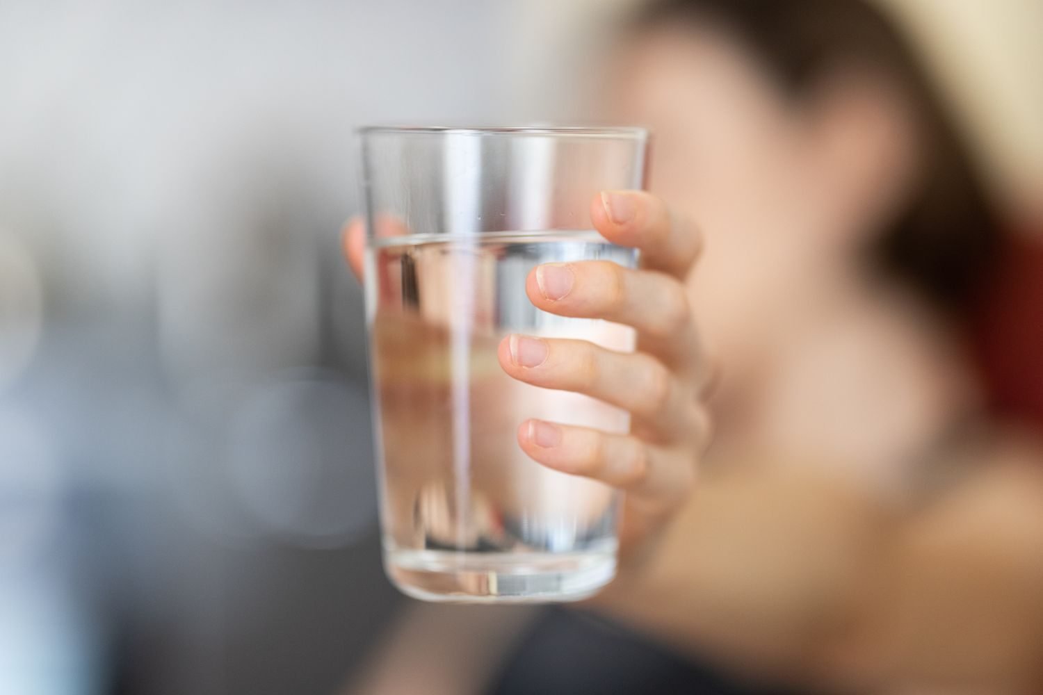 Person drinking a glass of water at a desk, illustrating hydration habits for migraine prevention