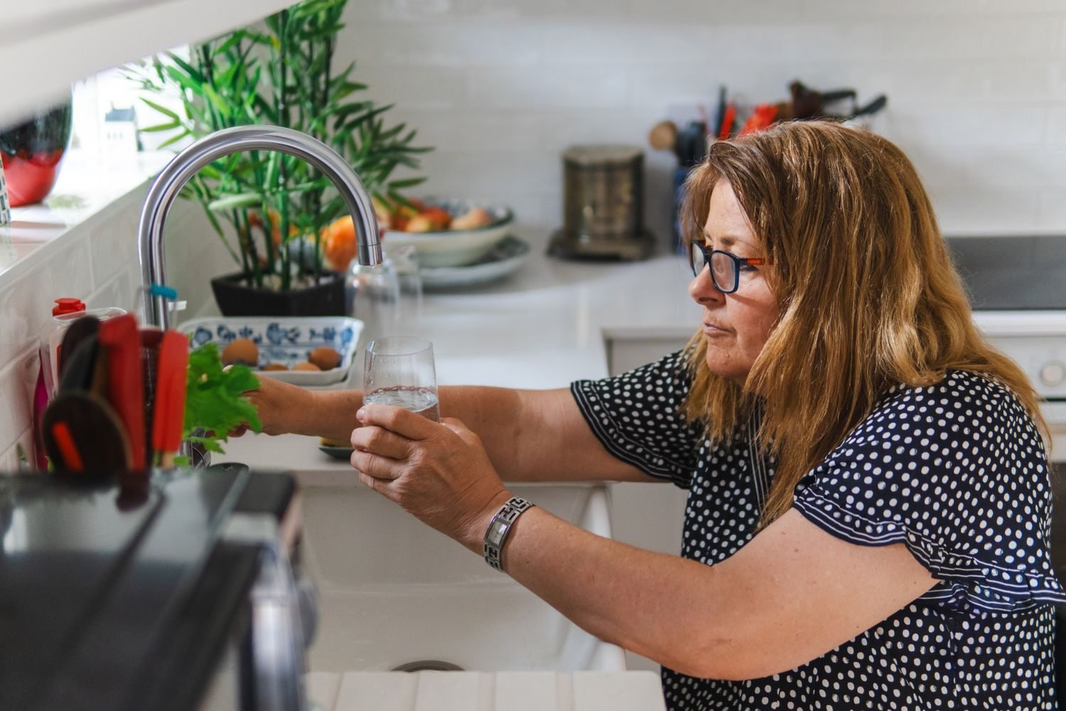 Person filling a glass with water at the kitchen sink, illustrating everyday hydration habits