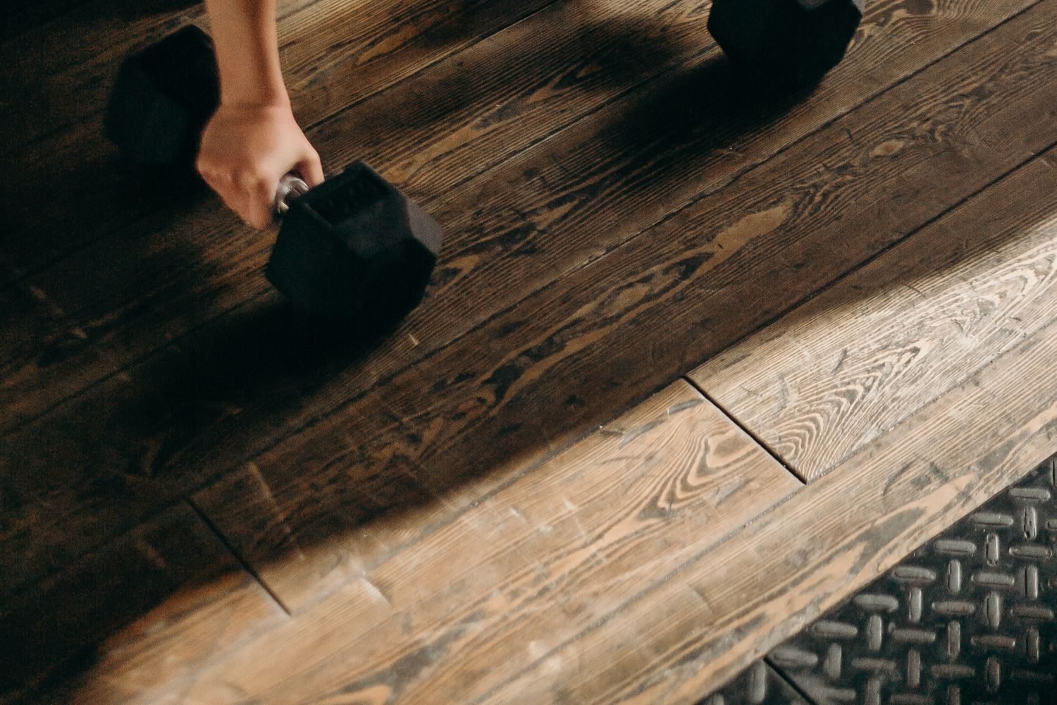 Hand holding a dumbbell on a wooden floor during a home workout
