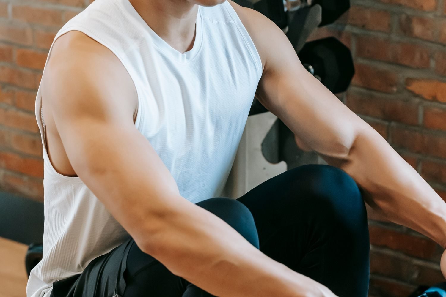 Man in a tank top seated near a dumbbell rack during a training session