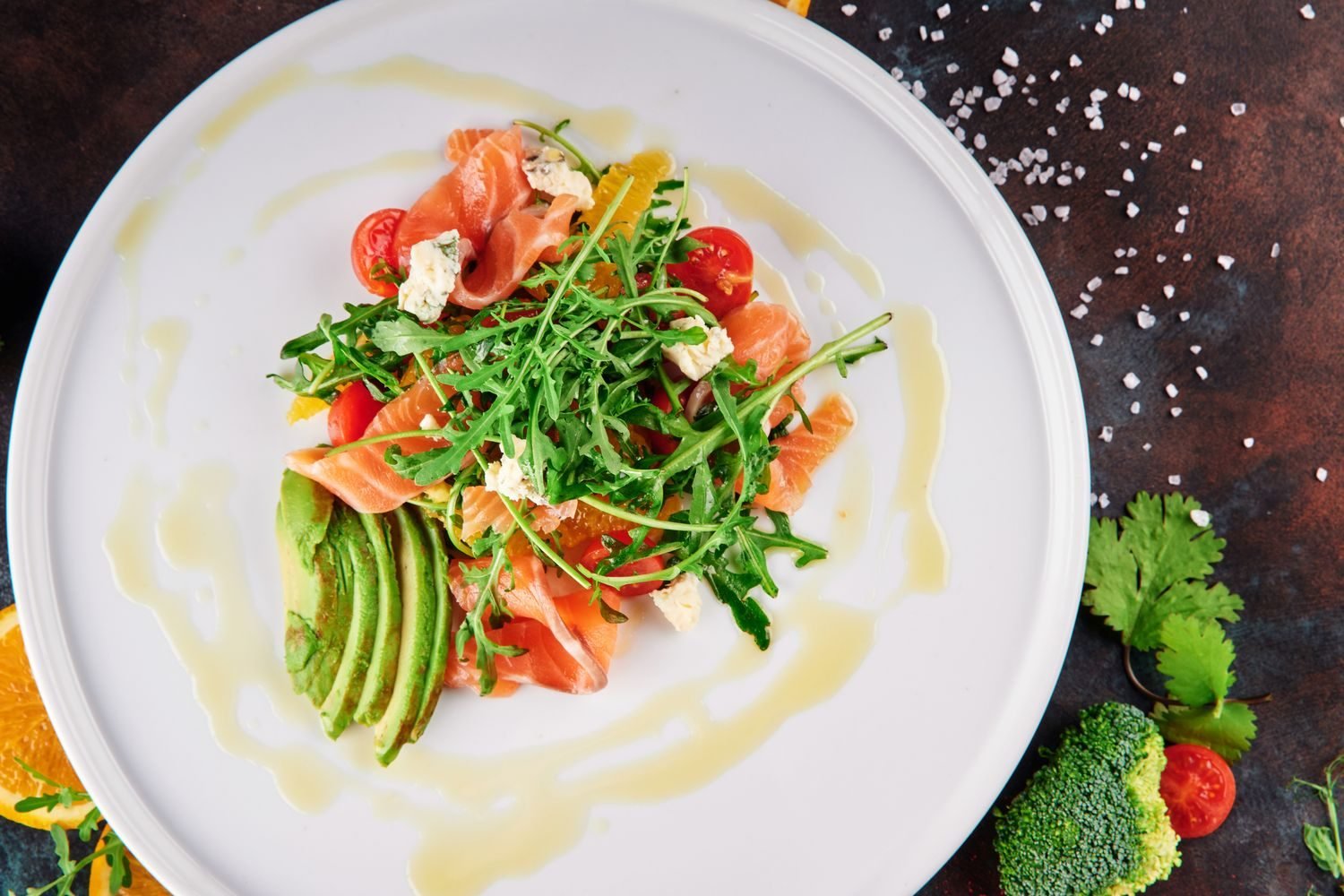 Plate with salmon, avocado, olive oil, and leafy greens representing protein and healthy fat sources for hormone synthesis