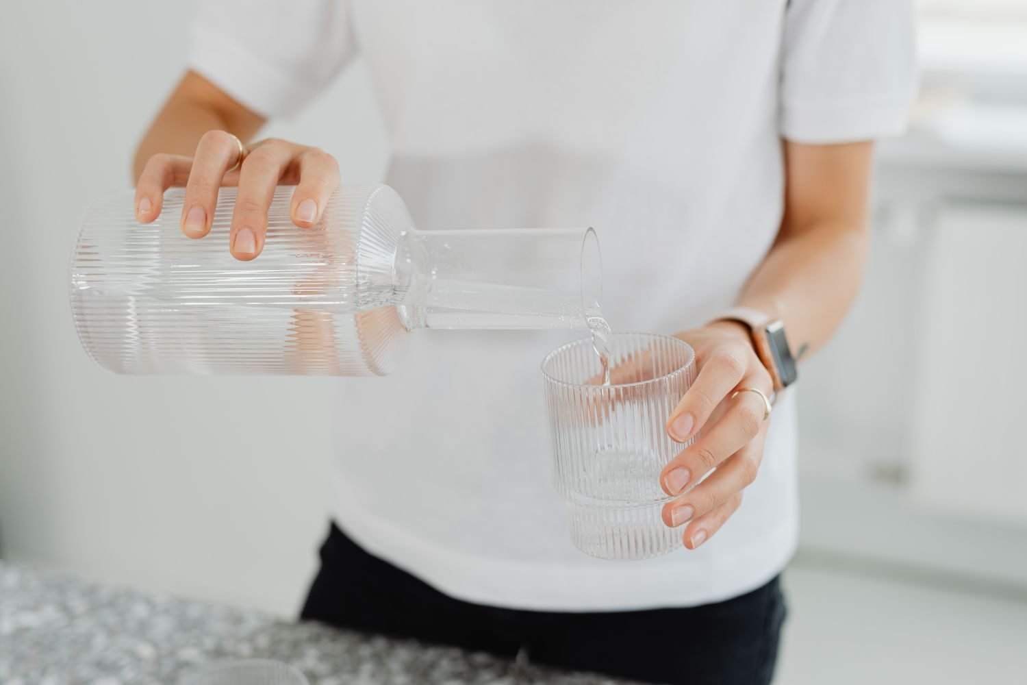 Person pausing to drink a glass of water before deciding whether a craving is really hunger or thirst