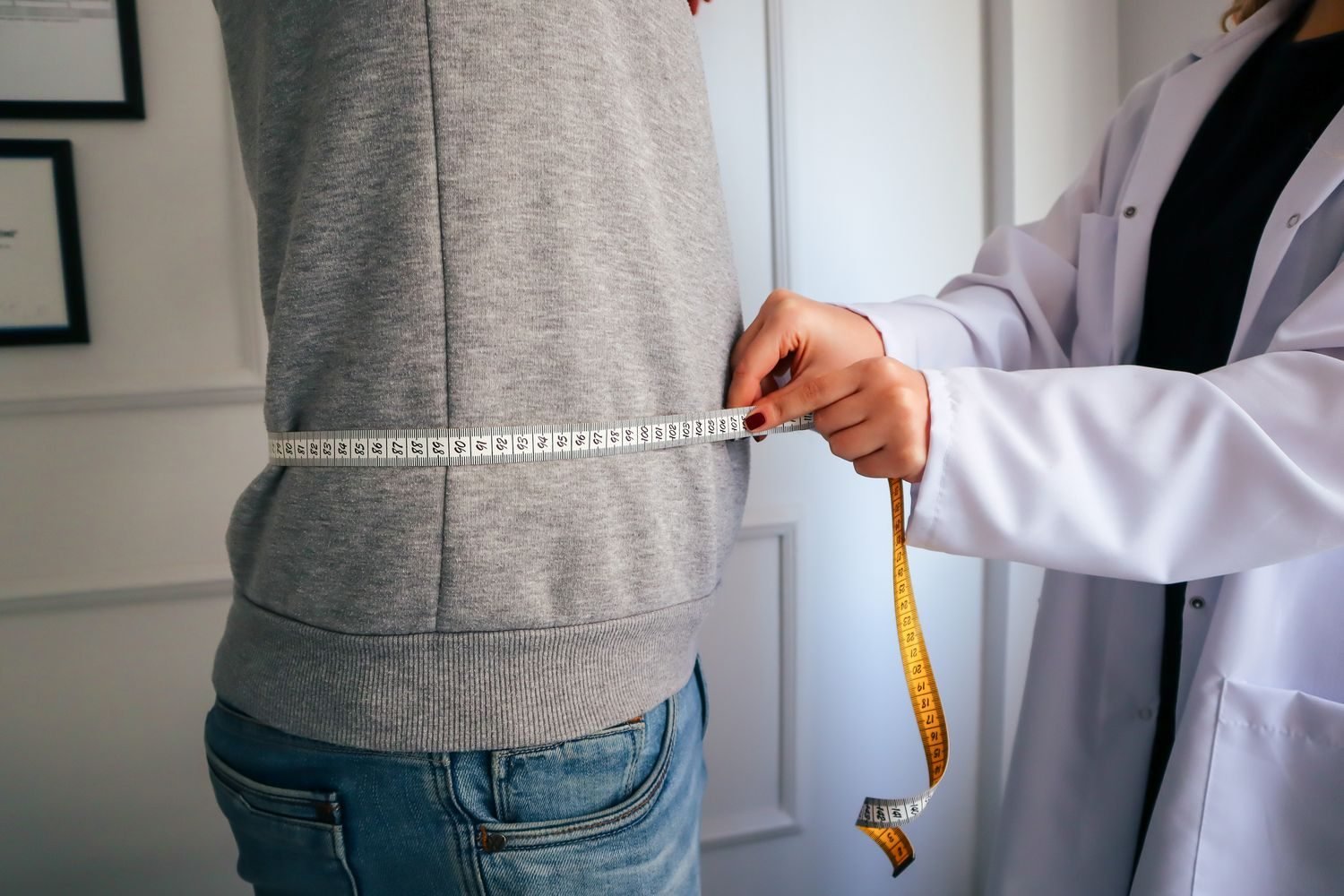 Person measuring waist circumference with a tape measure to track visceral fat progress