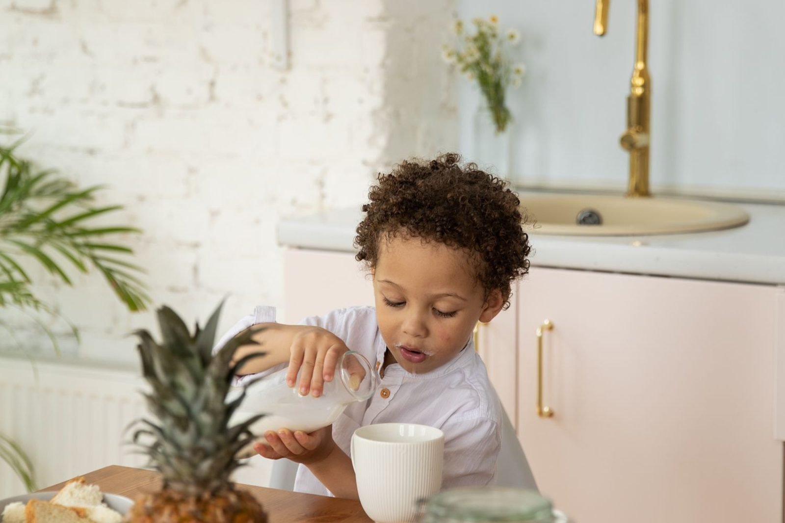 Child drinking a glass of plain milk at the breakfast table with fresh fruit alongside
