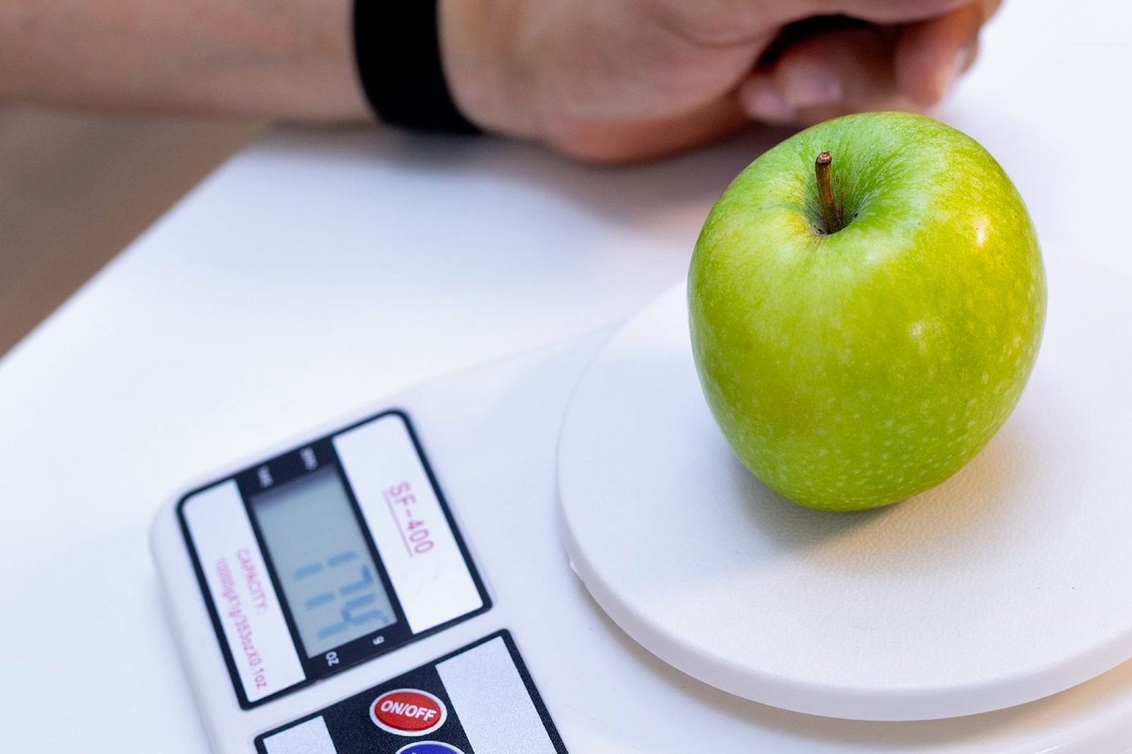 Person using a food scale and smartphone app to count carbohydrates in a meal for diabetes management