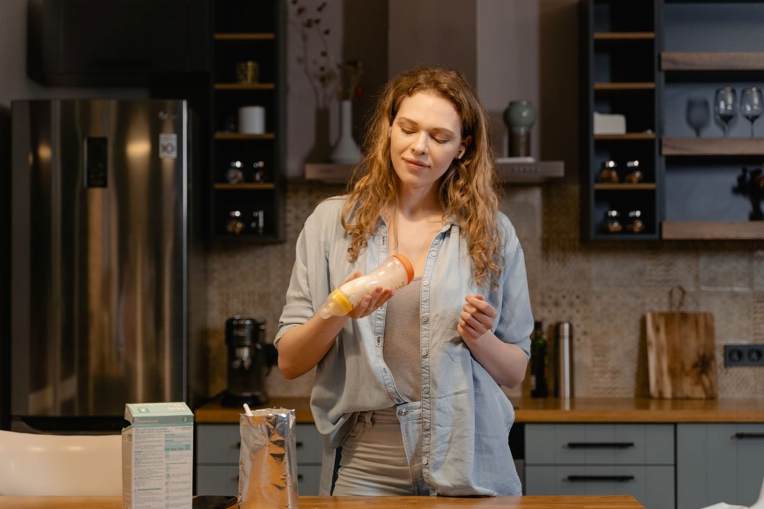 Parent preparing a bottle of formula while another bottle of expressed breast milk sits nearby