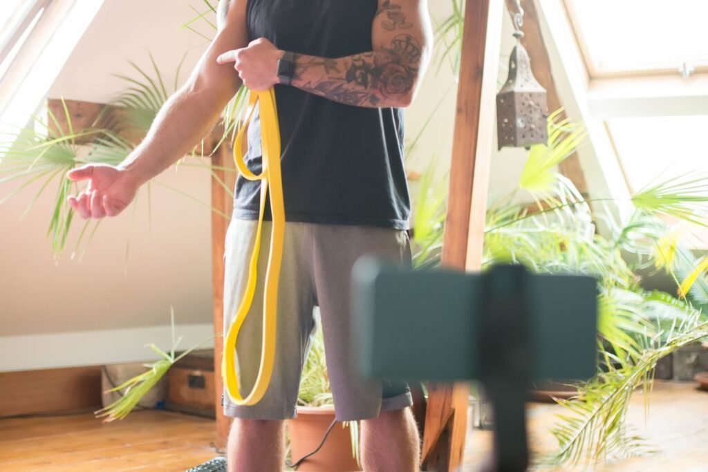 Man using a resistance band during a home workout in front of a propped-up phone