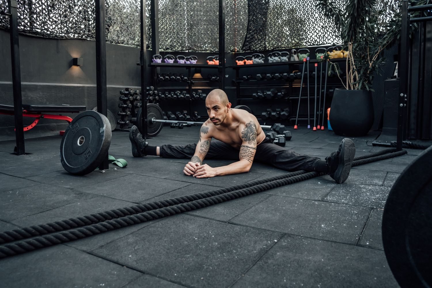 Man stretching on the floor of a gym surrounded by weights