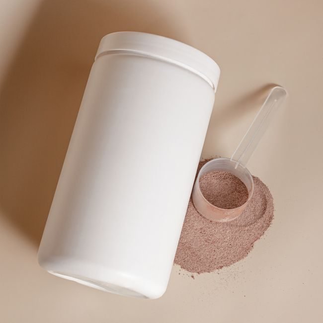 Tub of protein powder with a scoop of powder spilling out beside it