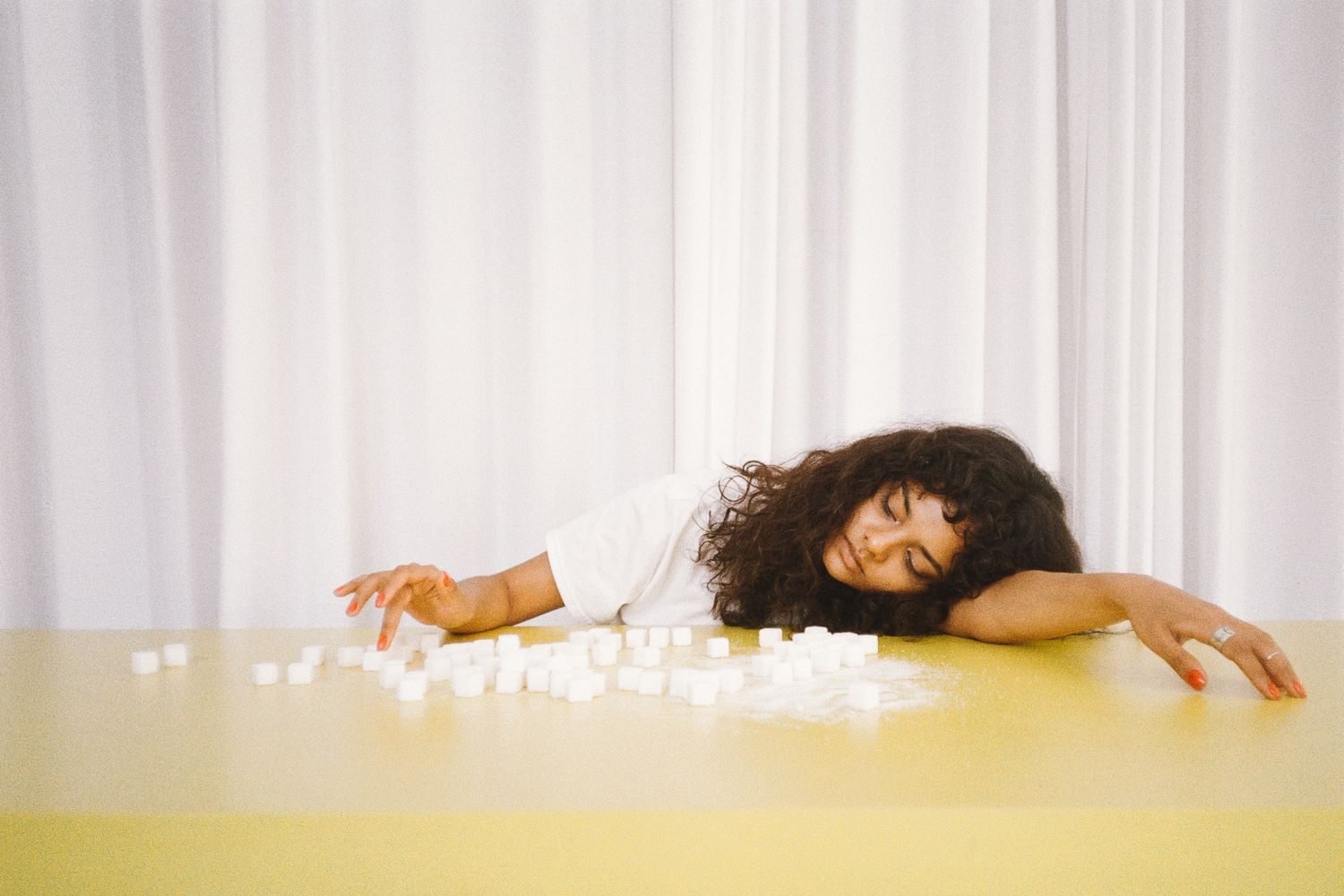 Tired woman resting head on desk next to empty coffee cup and sugary snack wrapper, showing an afternoon energy crash