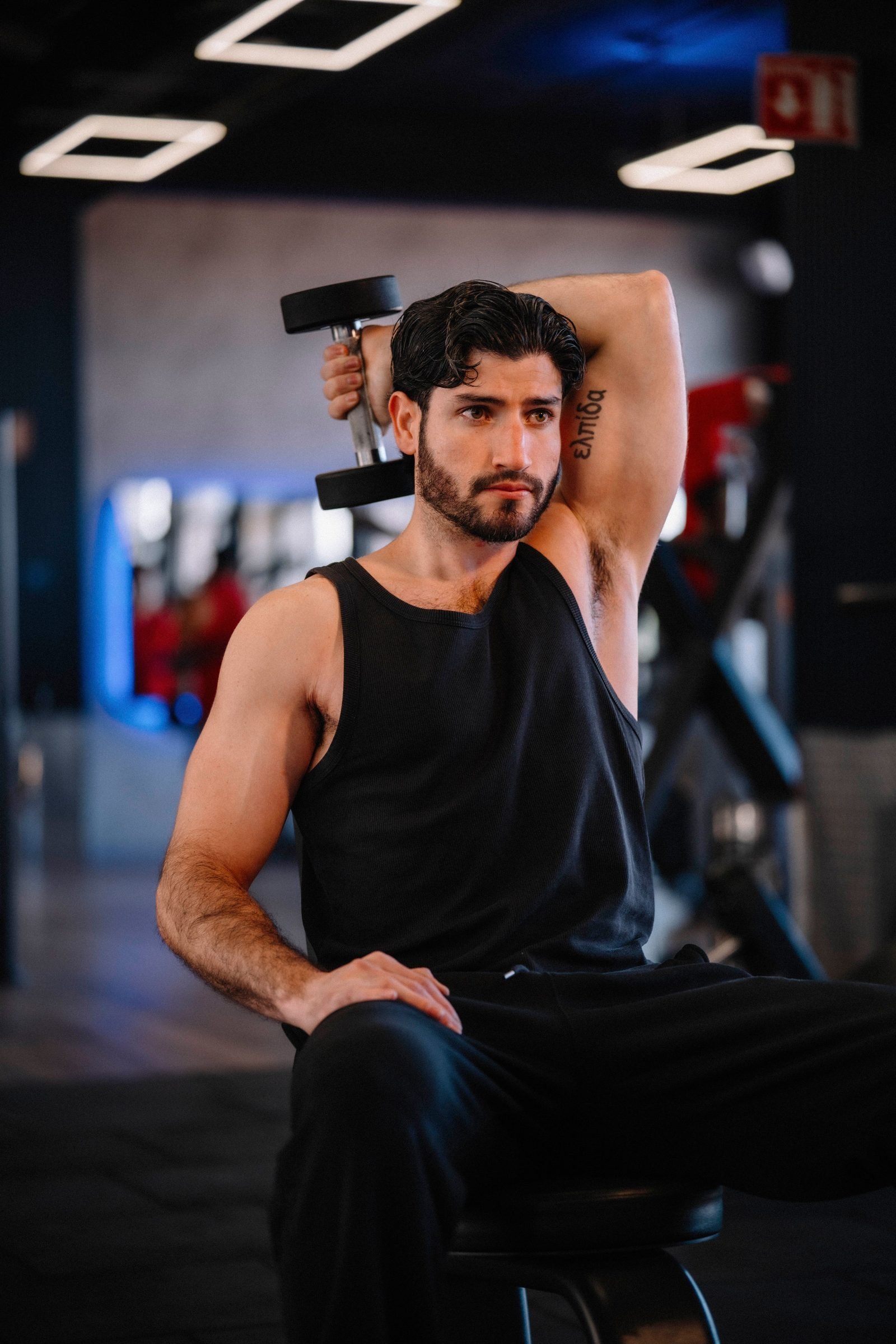 Man performing an overhead dumbbell tricep extension, a skull crusher variation, at the gym