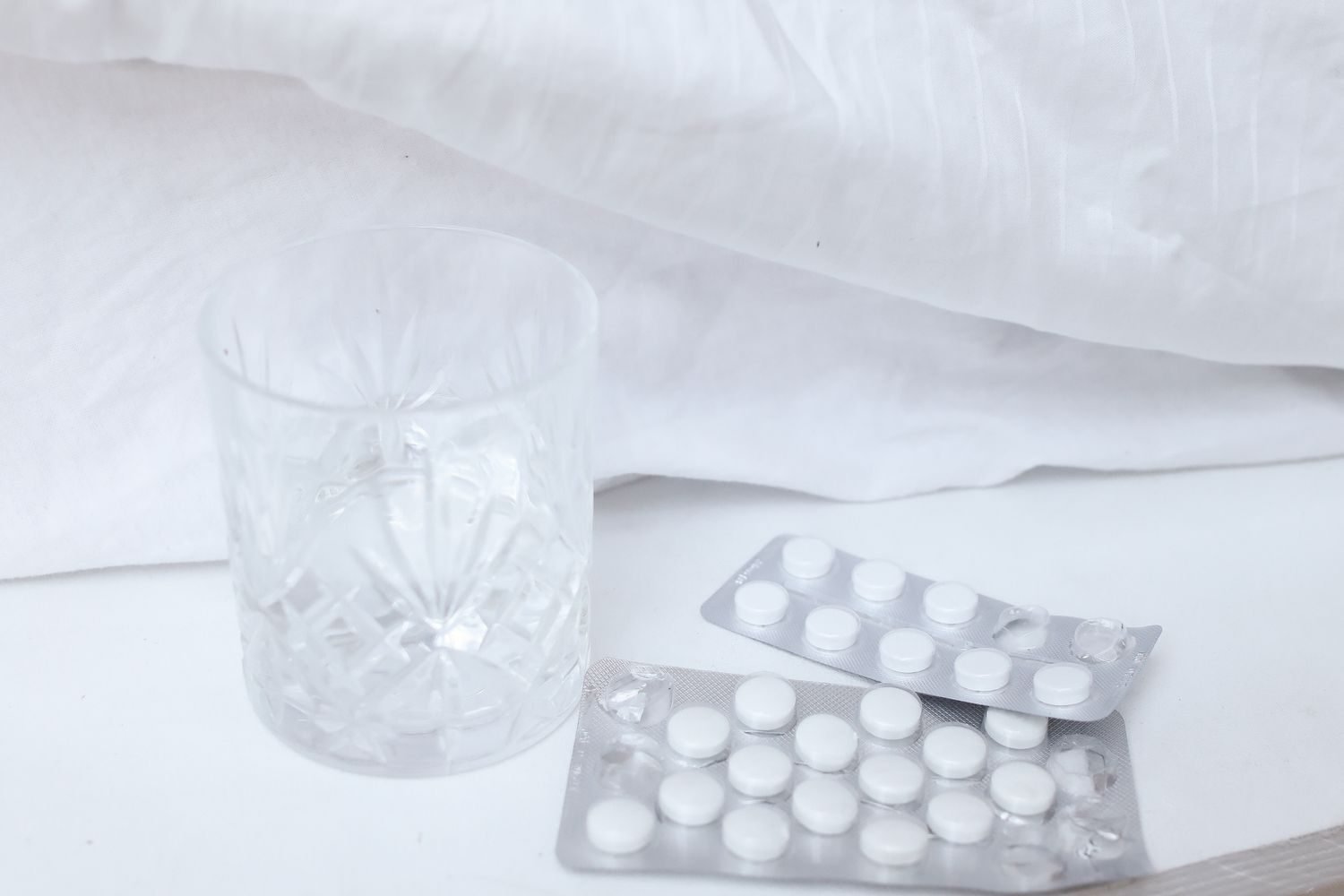 Glass of water and levothyroxine pill on a nightstand beside a clock showing early morning time