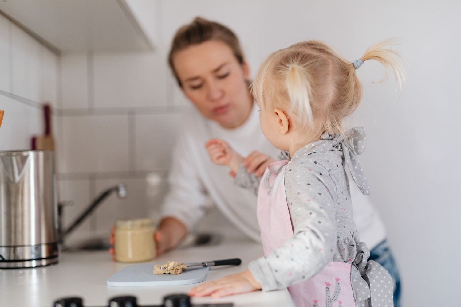 Toddler sitting at a table helping to stir a bowl of food during meal preparation, illustrating hands-on exposure to new foods