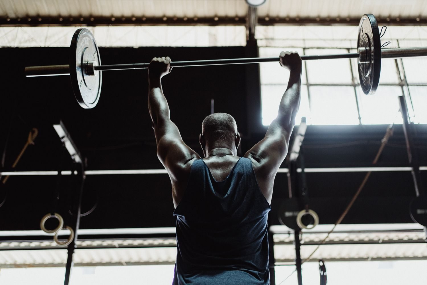 Man performing an overhead barbell press, back view showing trapezius engagement