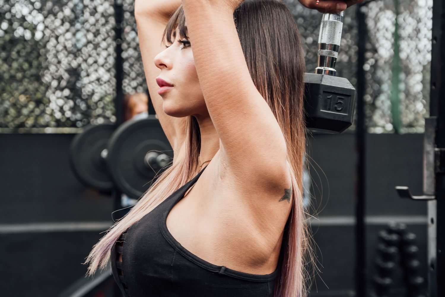 Woman performing an overhead dumbbell extension to target the tricep long head