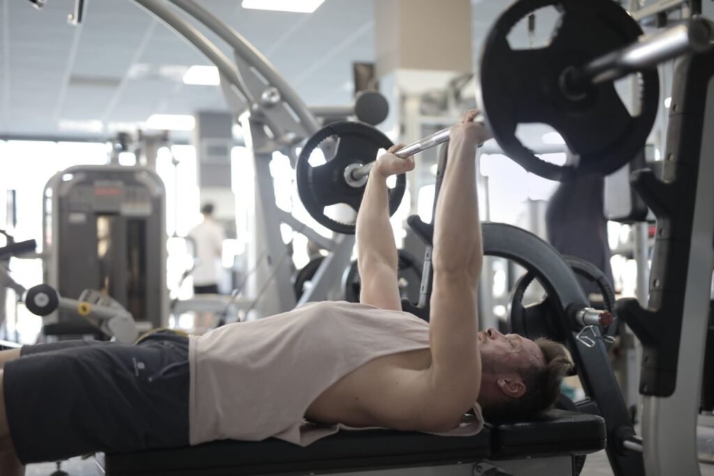 Man performing a barbell bench press lying on a bench in a commercial gym