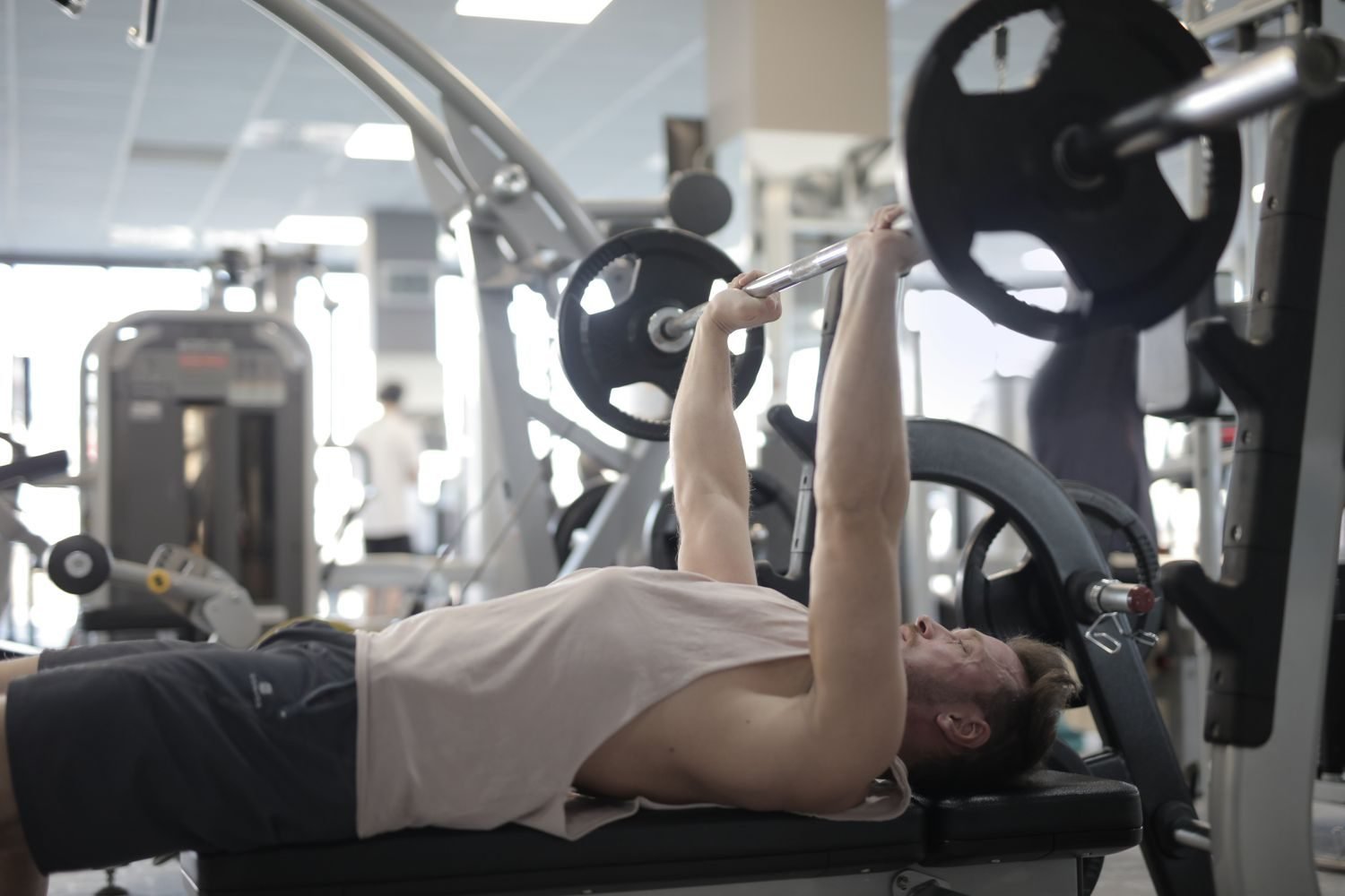 Man performing a barbell bench press lying on a bench in a commercial gym