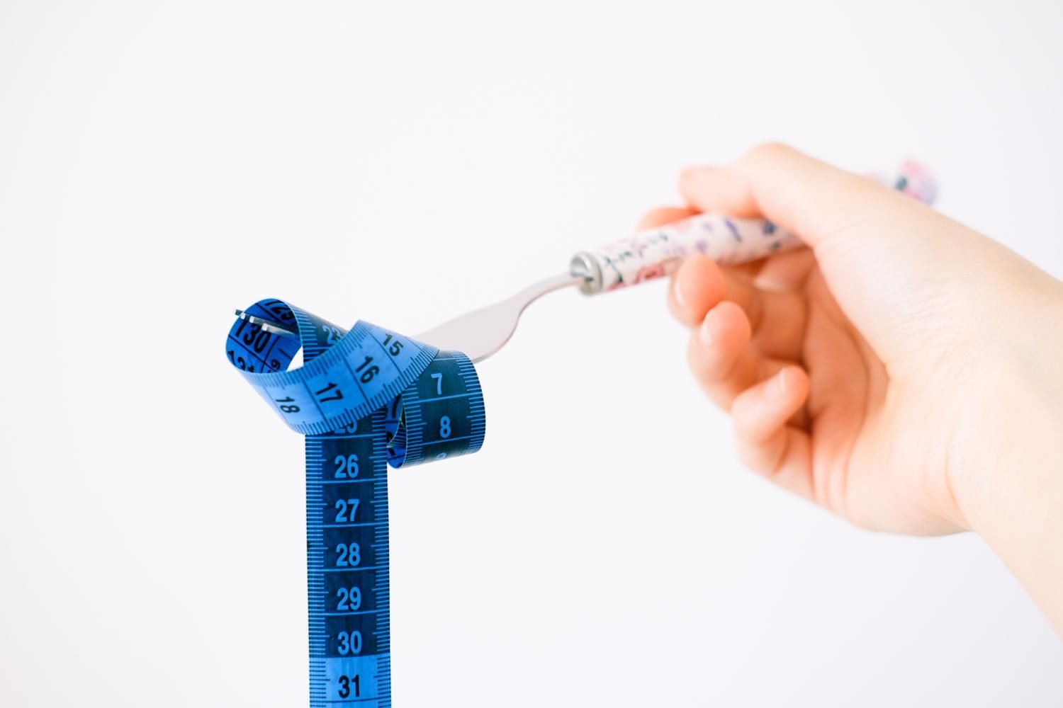 Hand holding a fork with a simple hunger and fullness scale illustration nearby, showing levels from hungry to full