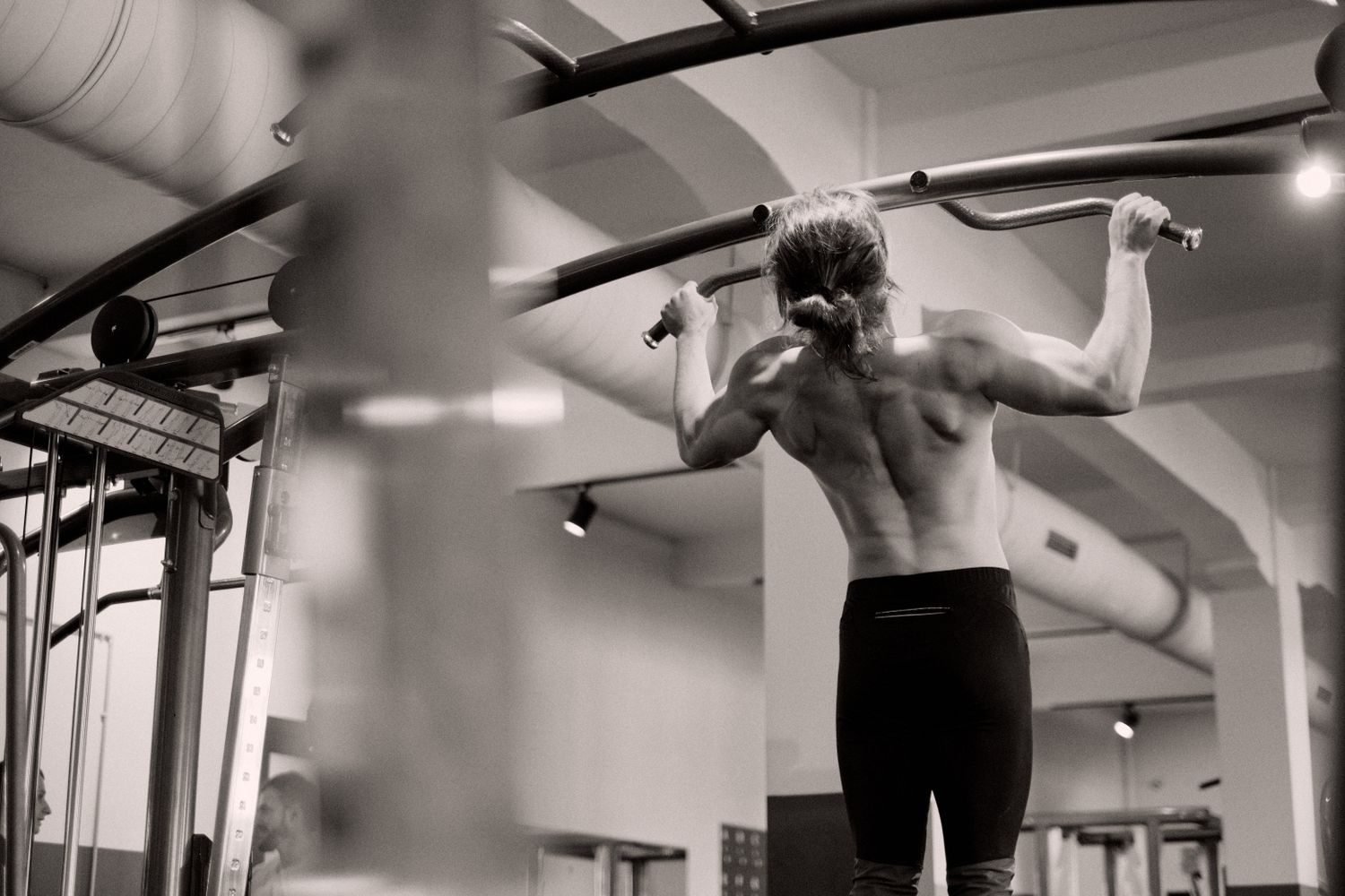 Man performing a wide grip pull-up at the gym, black and white photo