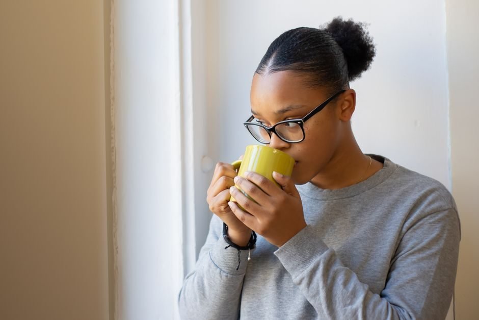 Woman drinking a cup of coffee by a window in the morning before training