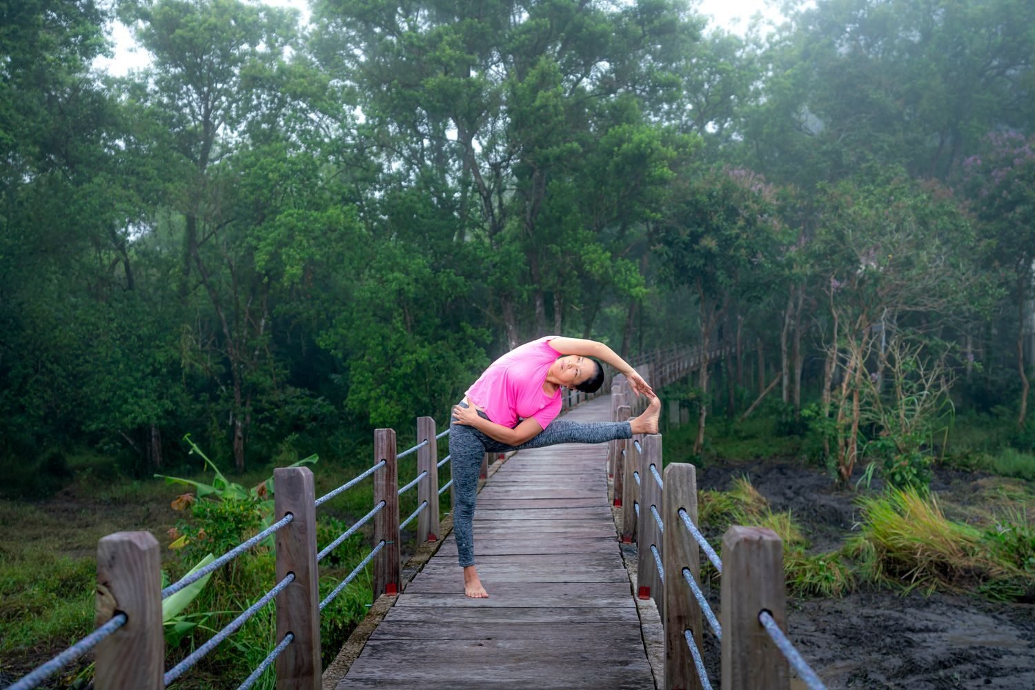 Woman stretching on a wooden bridge in a misty nature setting